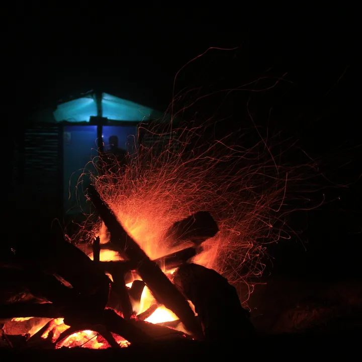 Ognisko nocą, w tle oświetlona chata
